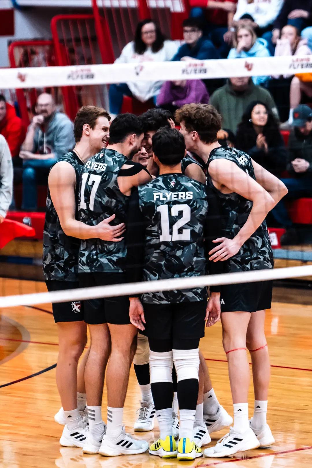 Volleyball team gathered in a huddle beside the court