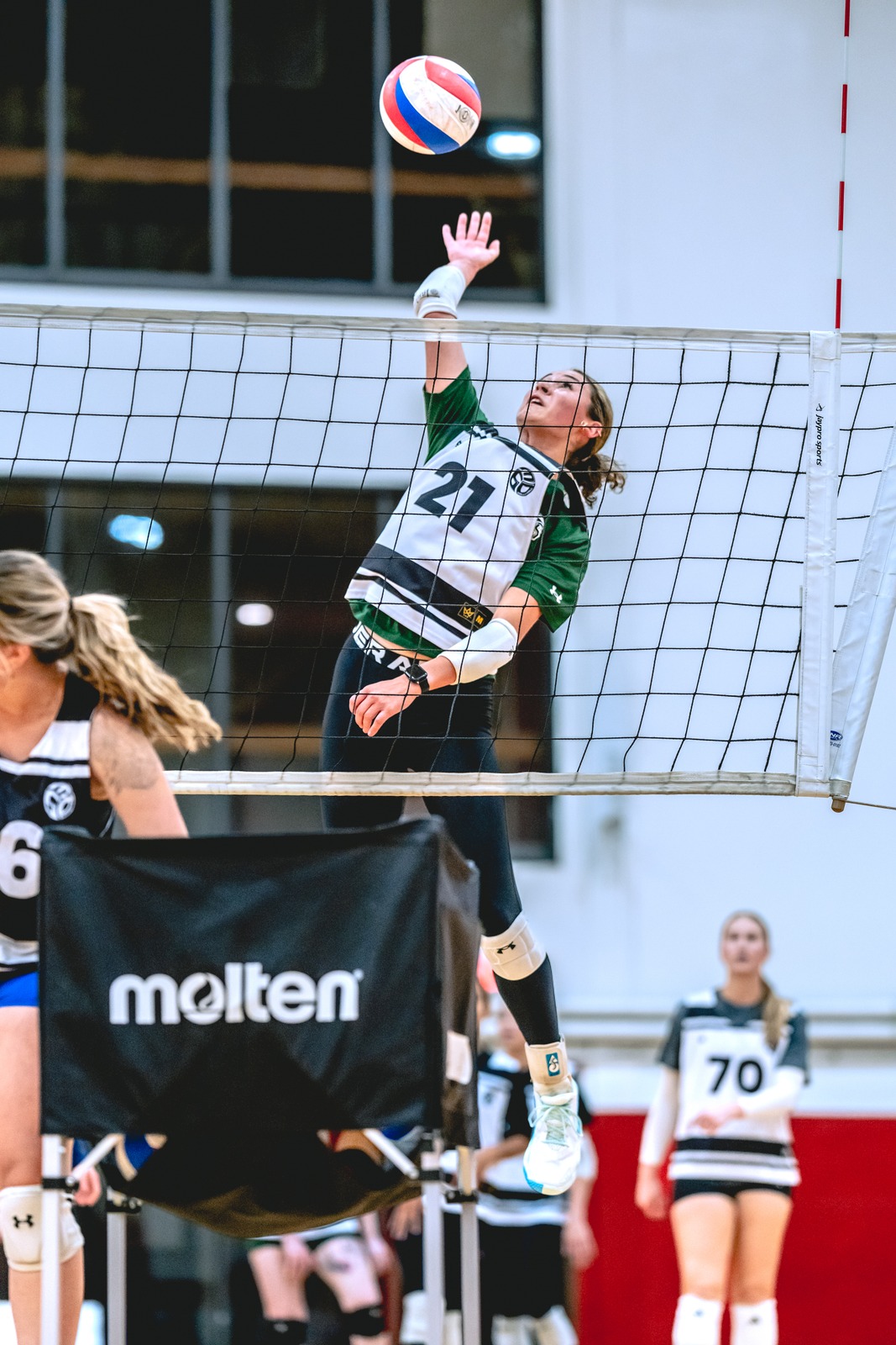 A player in a white and green top reaches overhead for the ball.