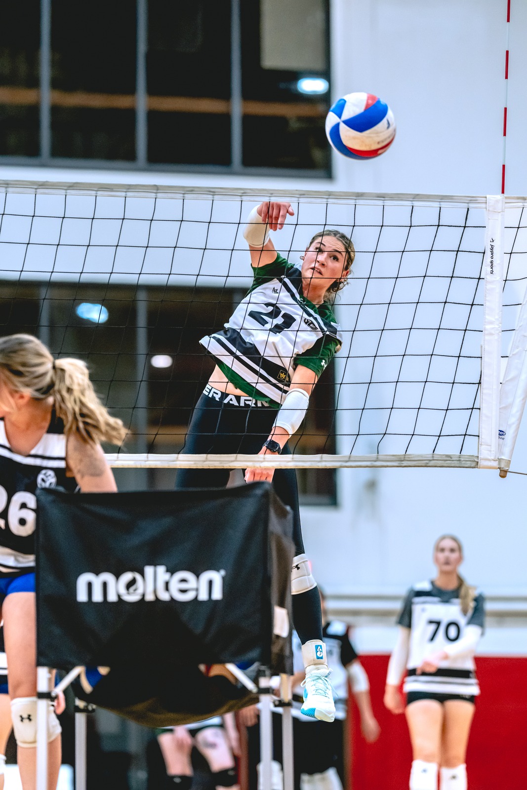 A player in a green and white top reaches for the ball over the net.