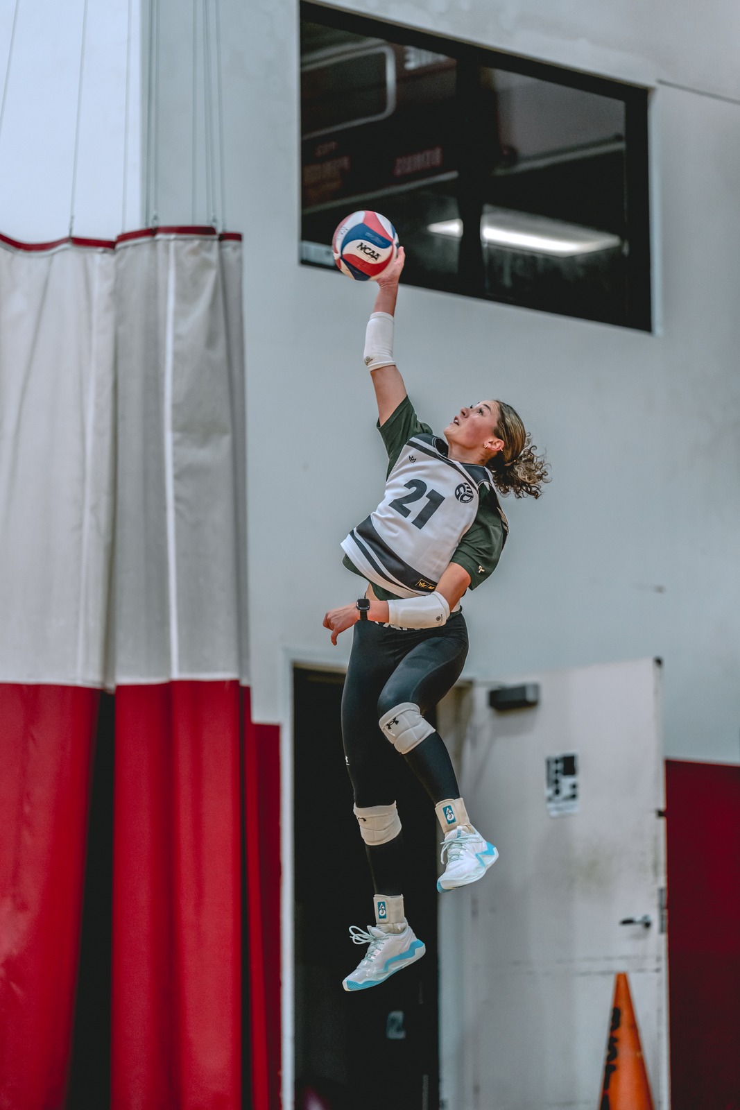 A player in a green top and white jersey jumps with a ball overhead.