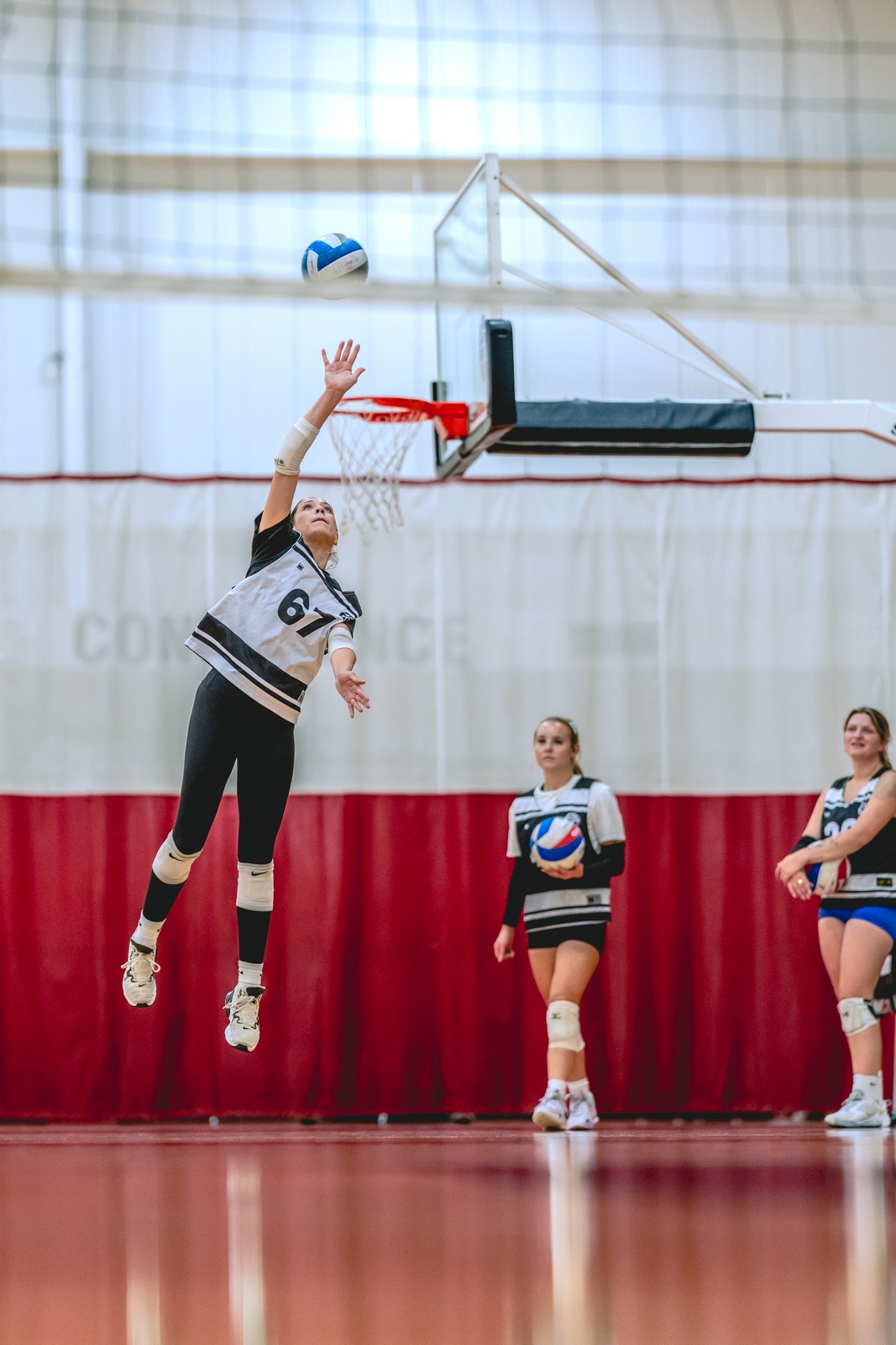 A player in a white and black uniform reaches up. Two other players in white and black uniforms stand on the court.