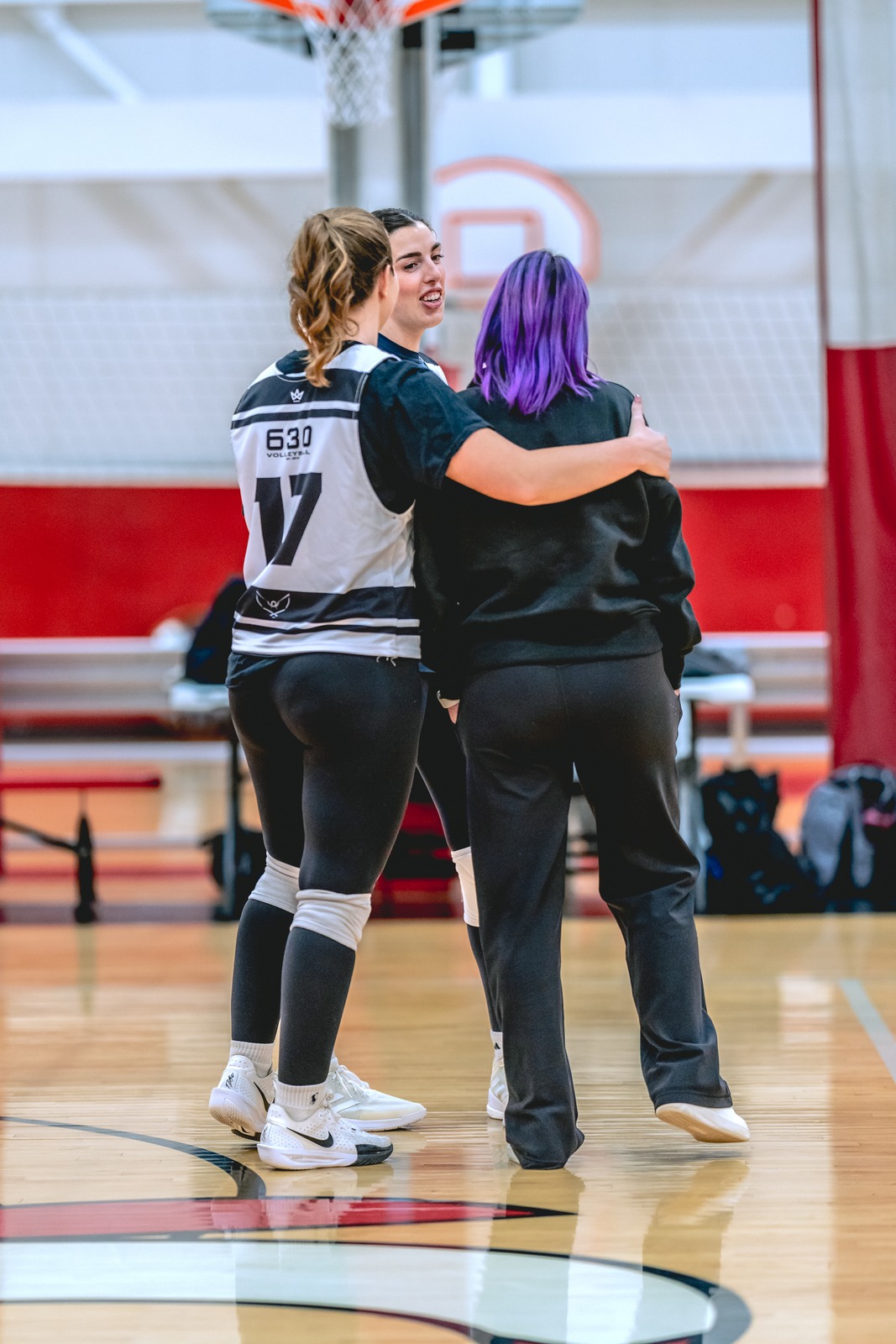Three players huddle on a court. One player in a black top has an arm around another player.