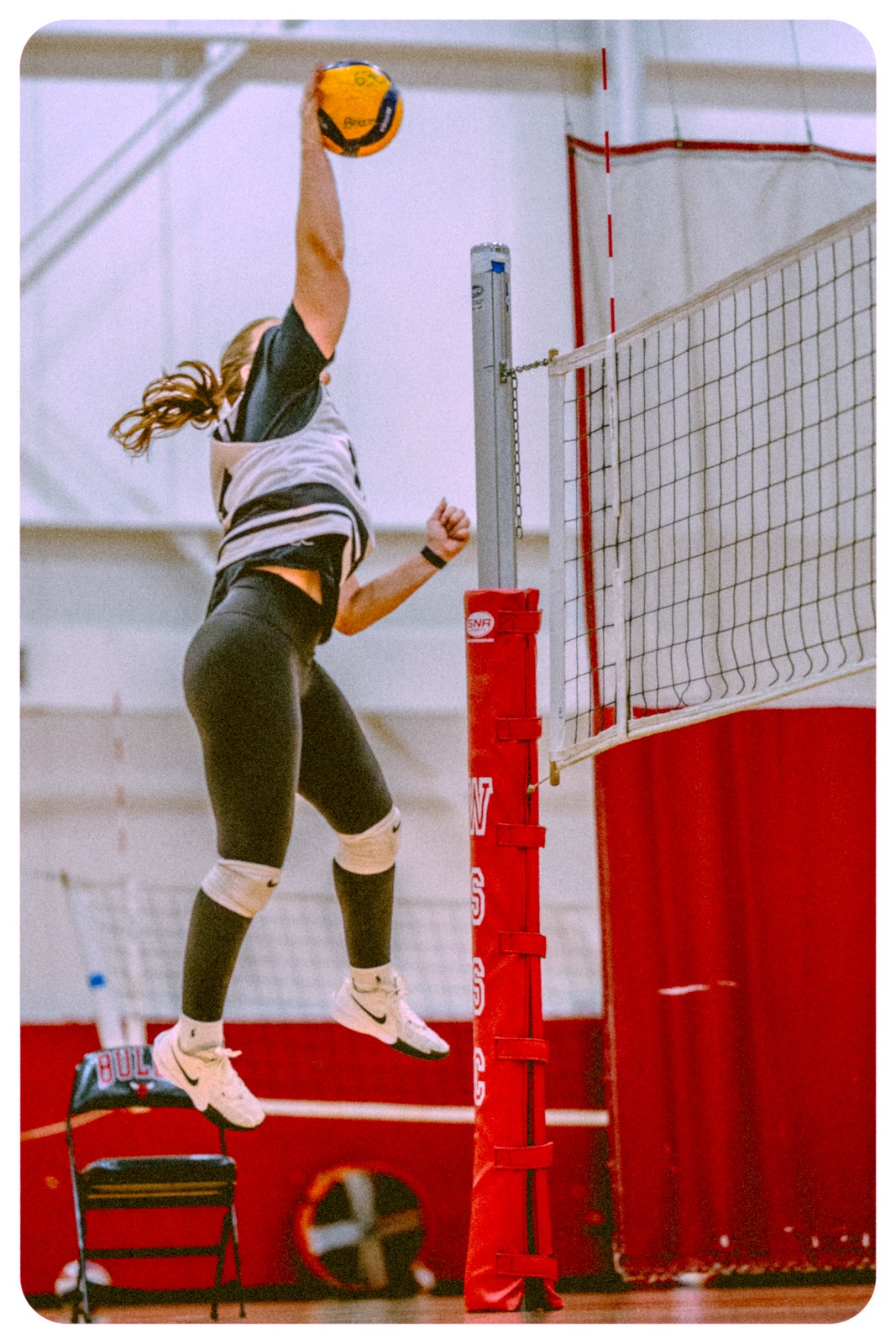A player in a black top and grey vest jumps with a volleyball.