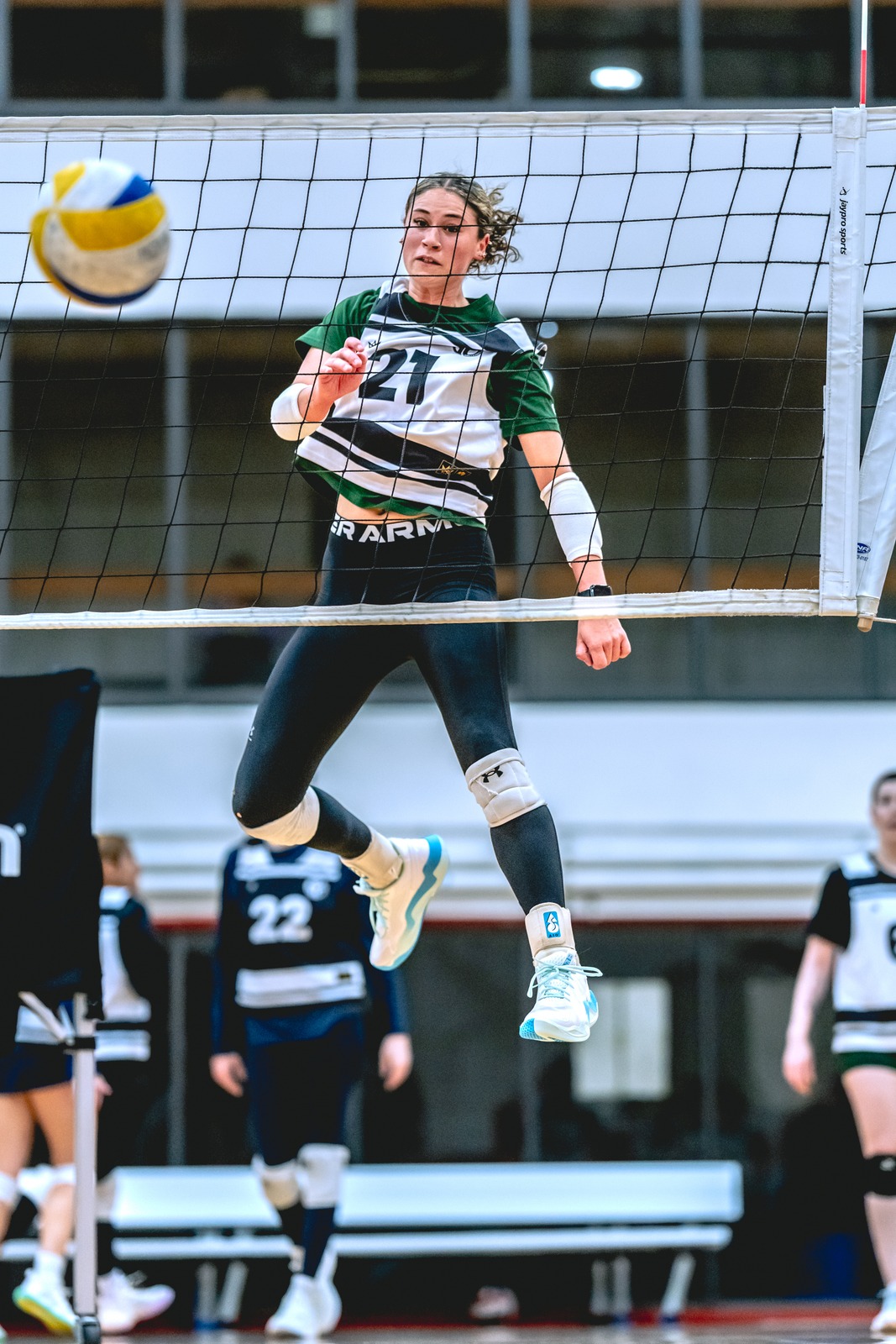 A player in green and white jumps near the net.