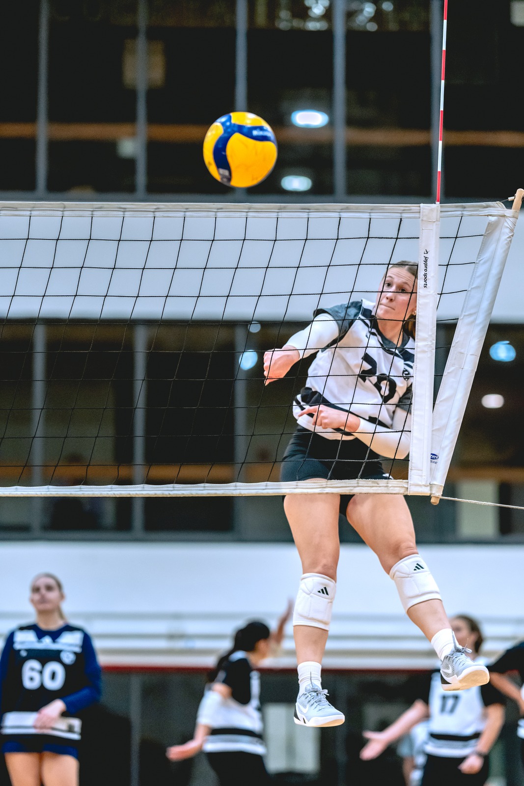 A player in a white and black top jumps near the net with a ball in the air.
