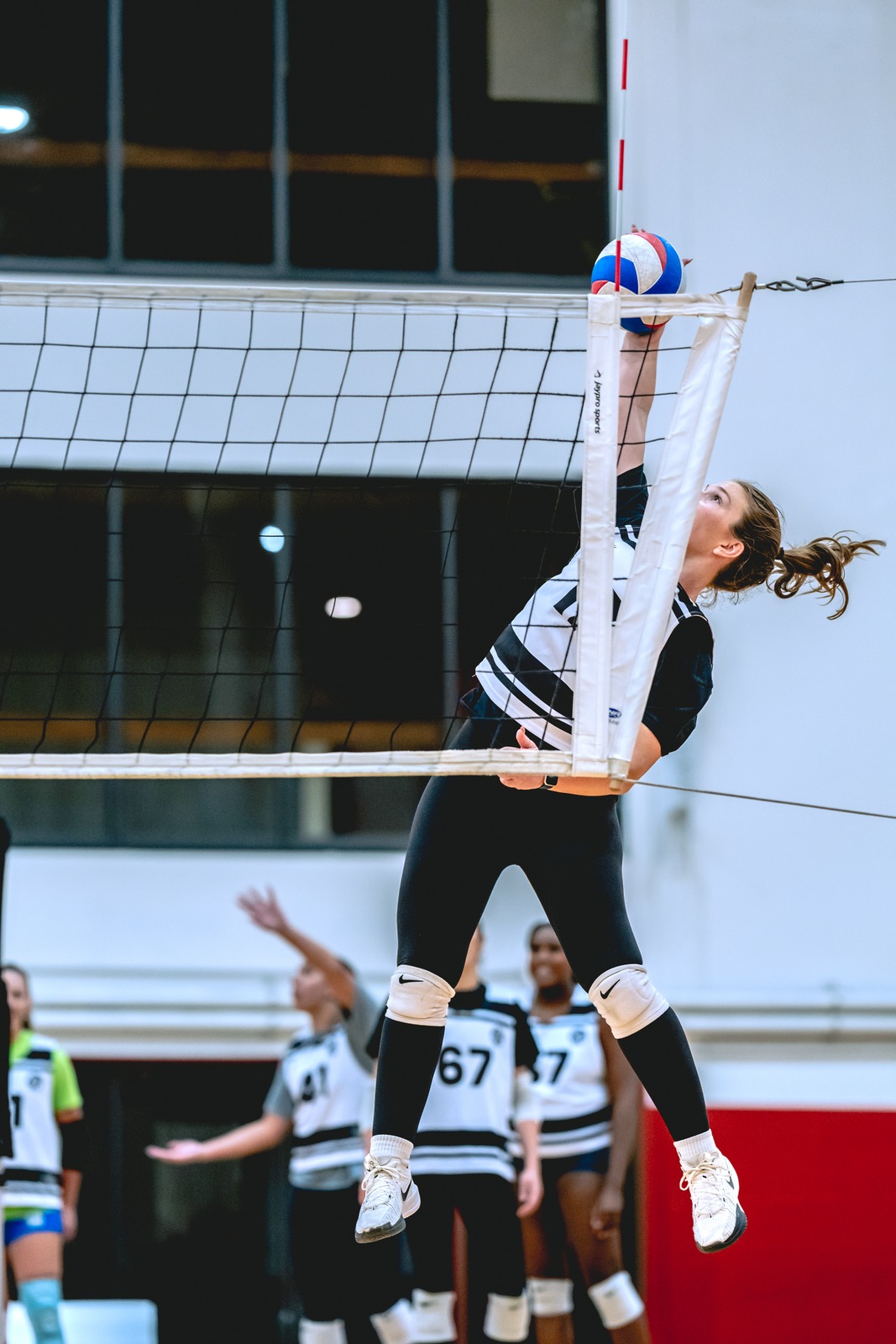 A player in black and white reaches overhead for the ball.