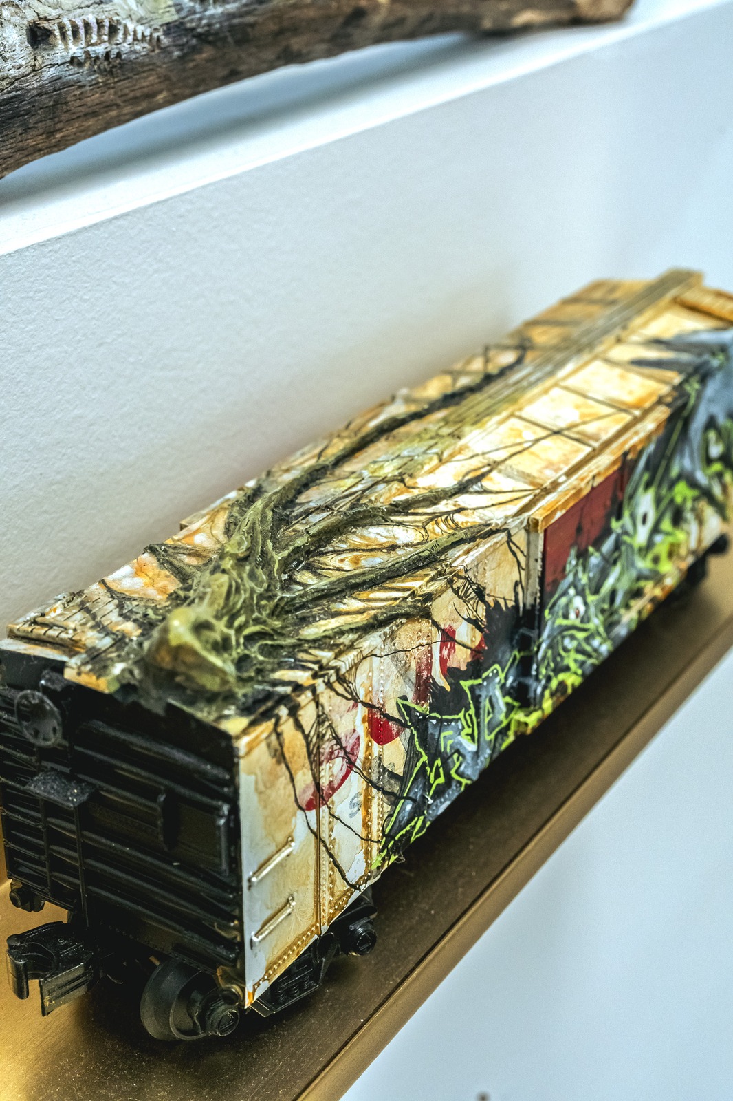 A detailed model train car with a textured, painted exterior rests on a shelf.