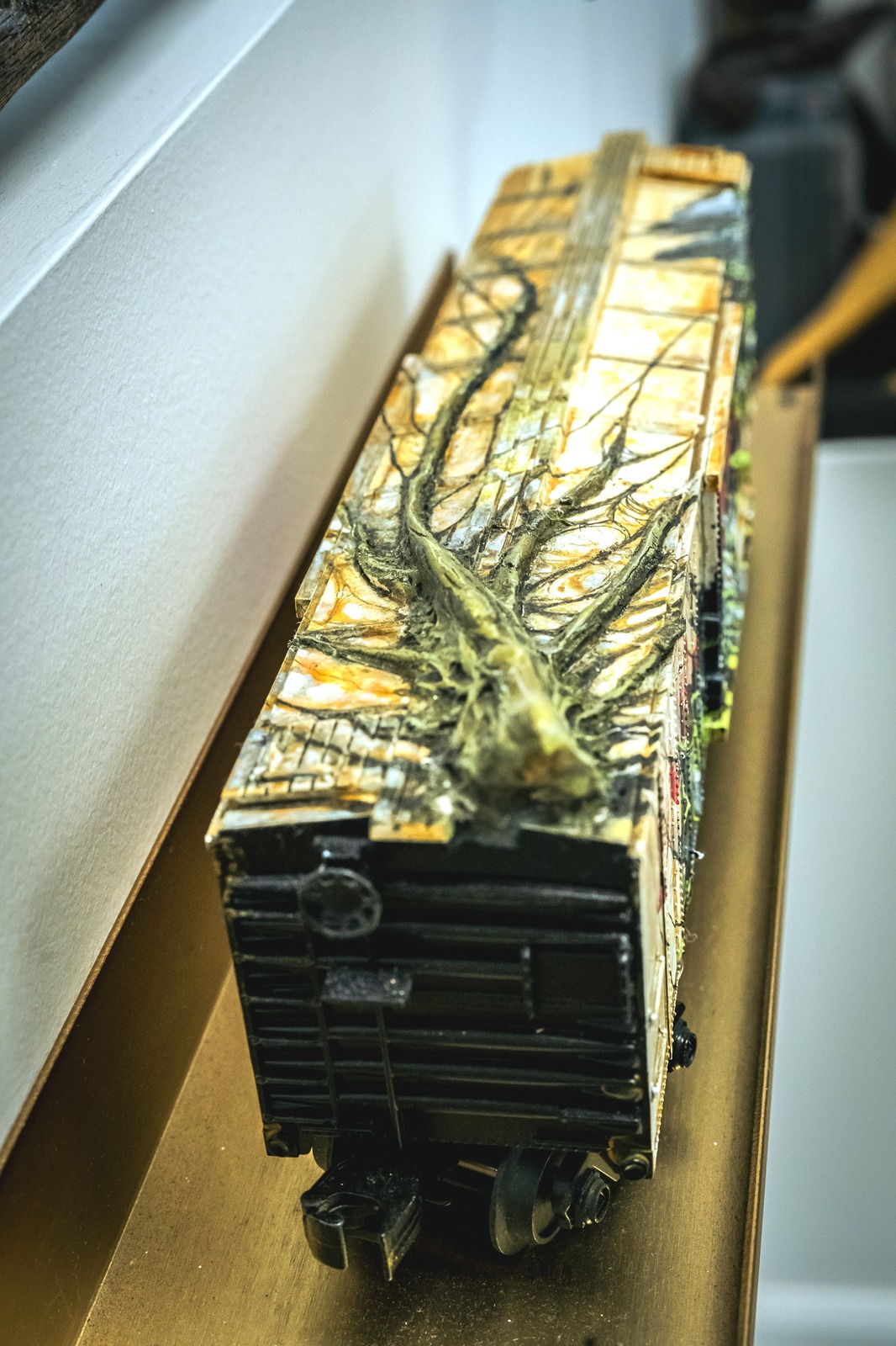 A miniature train car with a tree branch design sits on a golden surface.
