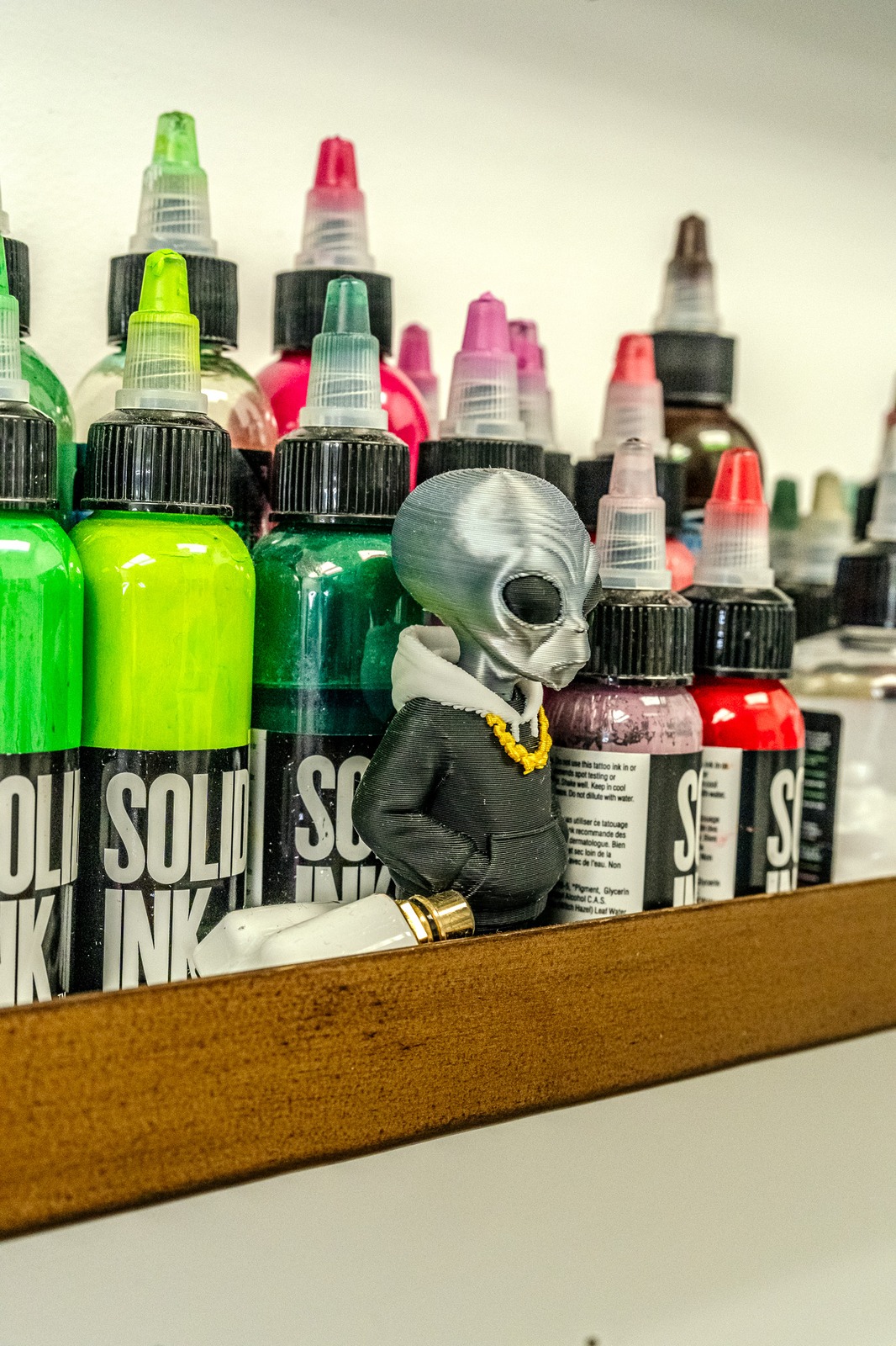 A figurine of an alien stands among bottles.
