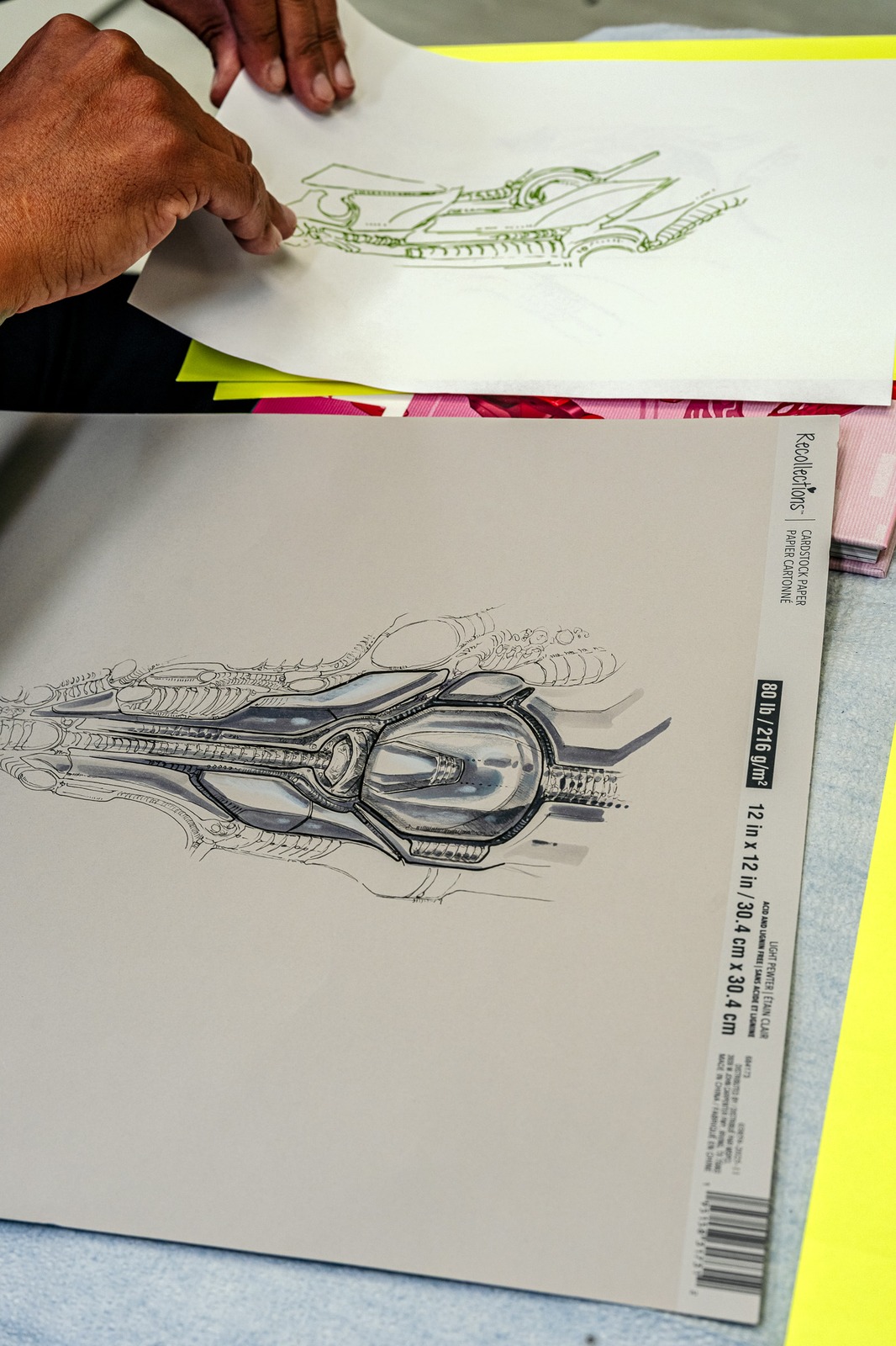 Hands hold a drawing of a futuristic vehicle.