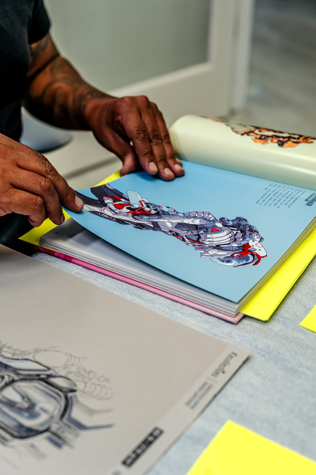 A person in a black shirt turns pages of a book displaying artwork.