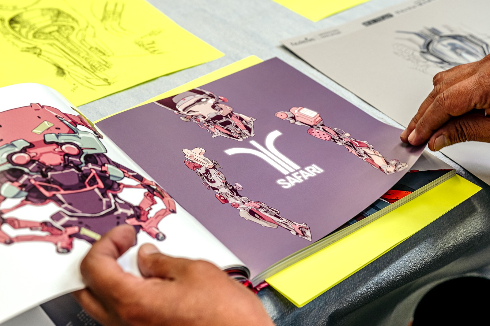 A person's hands turn pages of a portfolio with robotic illustrations.