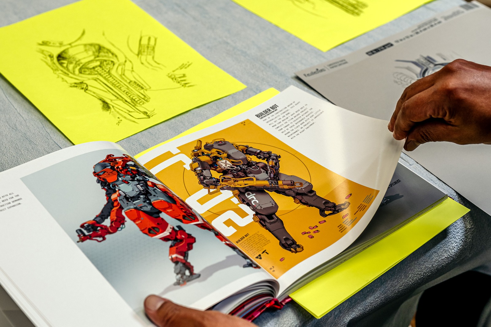 A hand turns a page in a book showing illustrations of robots.