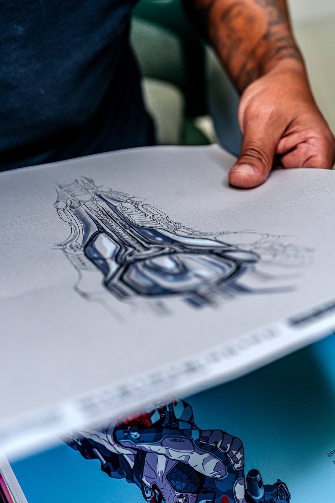 A person in a dark shirt holds a drawing of a mechanical object.