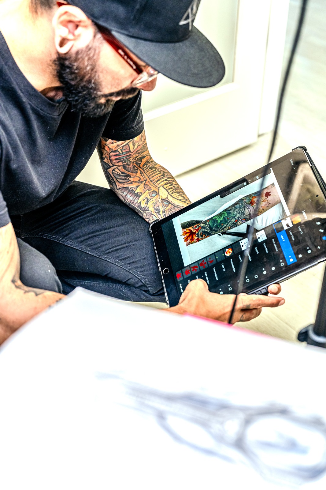 A person in a black shirt and black hat looks at a tablet displaying a tattoo design.