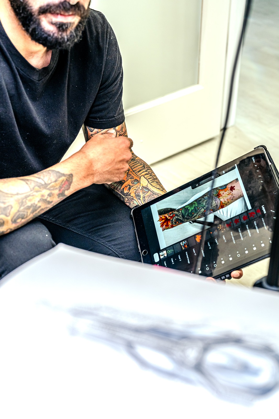 A person in a black shirt holds a tablet displaying a tattoo design.