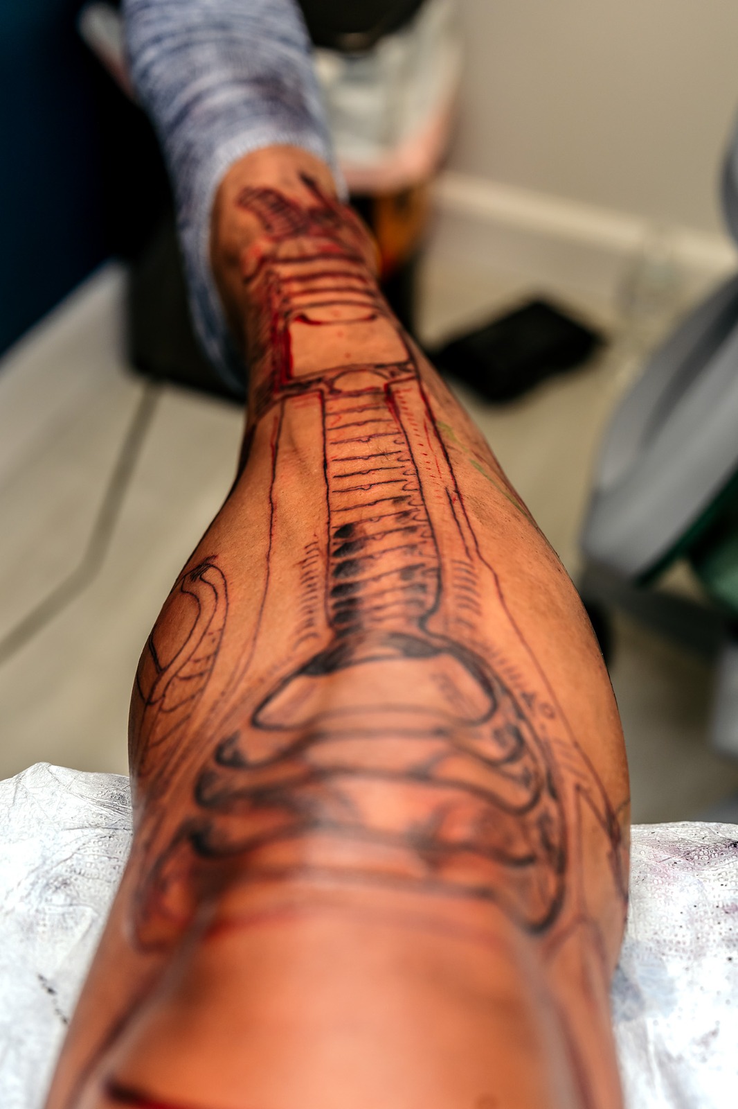 A person's leg is covered in black and red drawings of bones and mechanical parts.