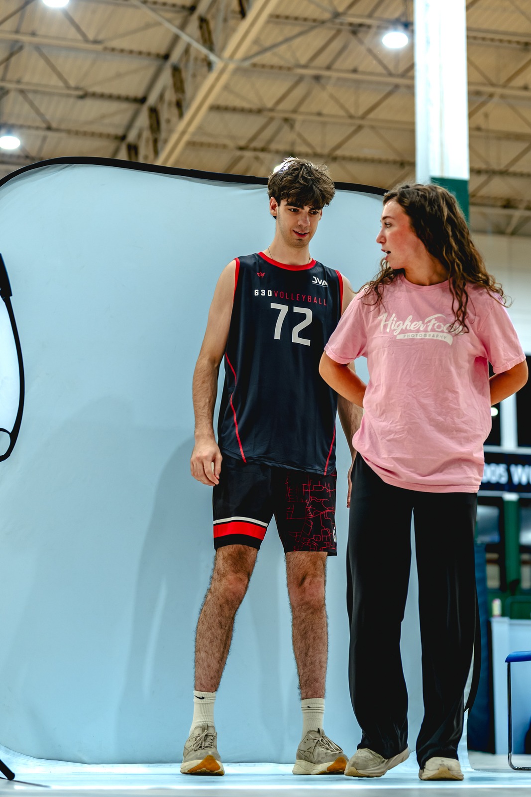 A player in black stands beside a person in pink at a photo backdrop.