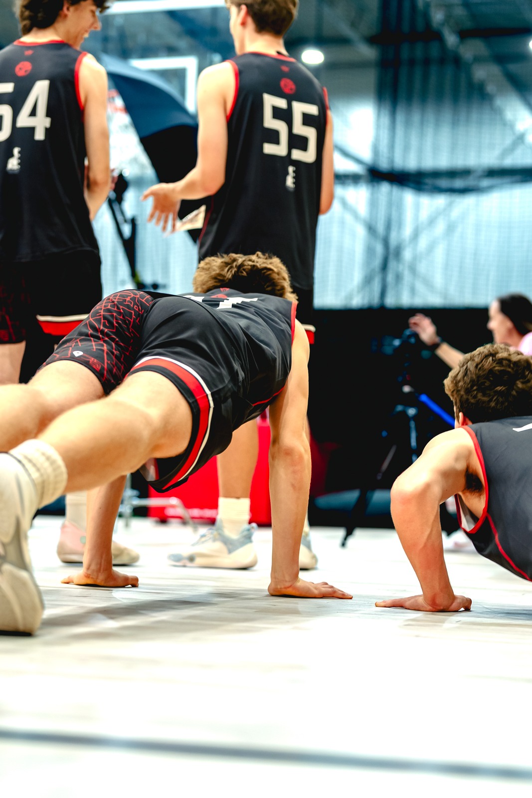 Players in black and red hold push-up positions on a photo backdrop while others stand behind.