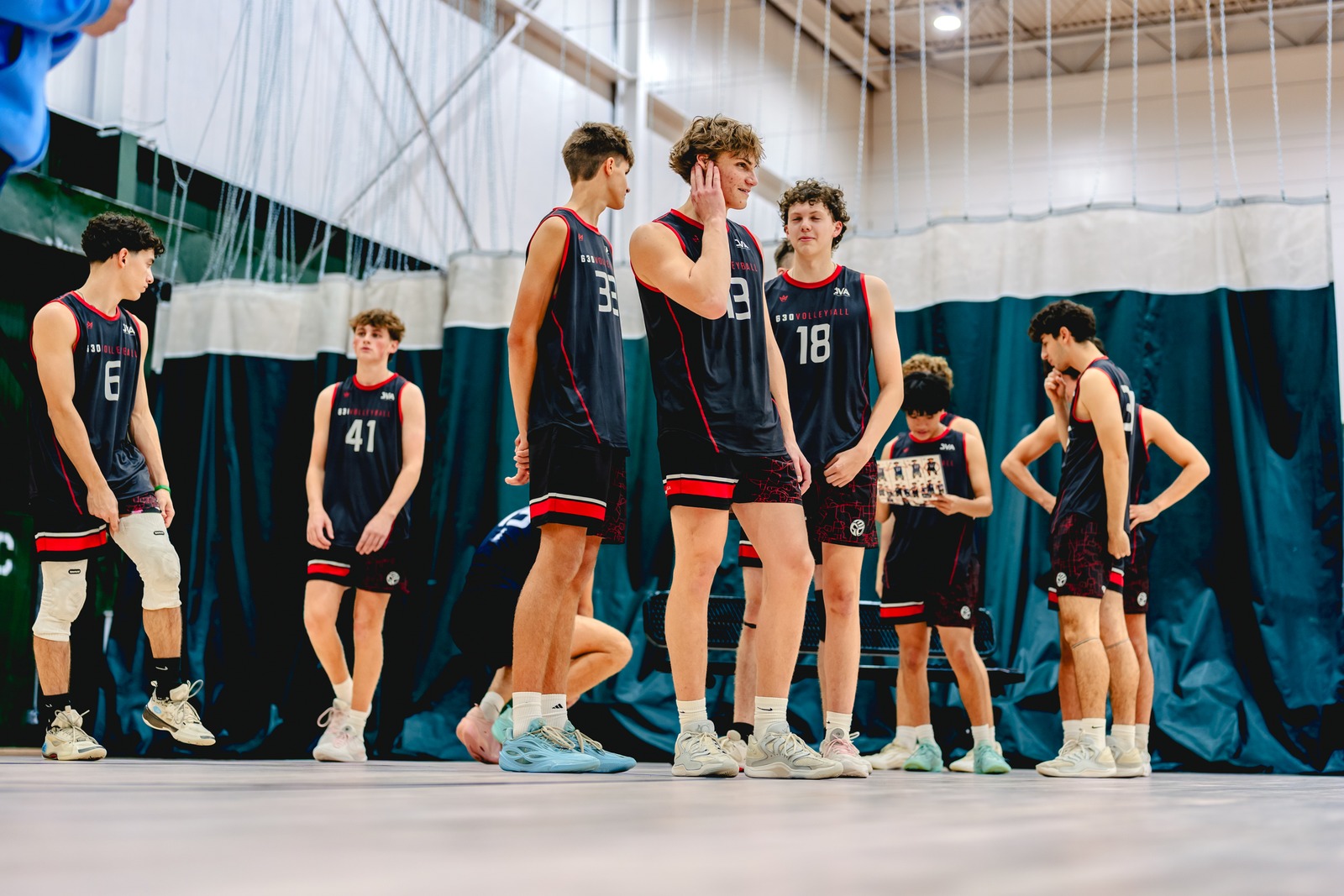 Players in black and red uniforms stand on a court.