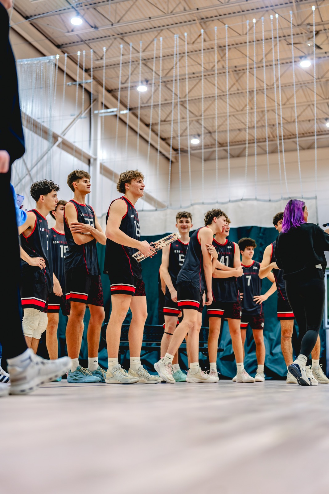 Players in black and red uniforms stand together on a court.