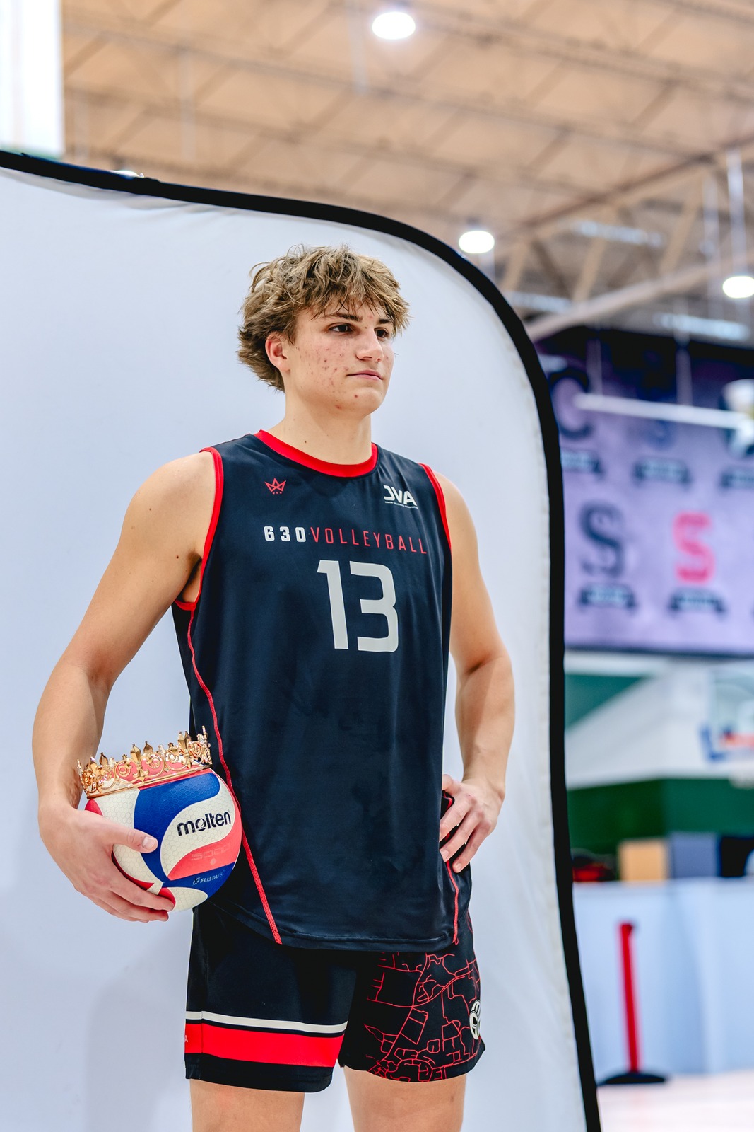 A player in a black top and shorts stands with hands on hips, holding a volleyball.