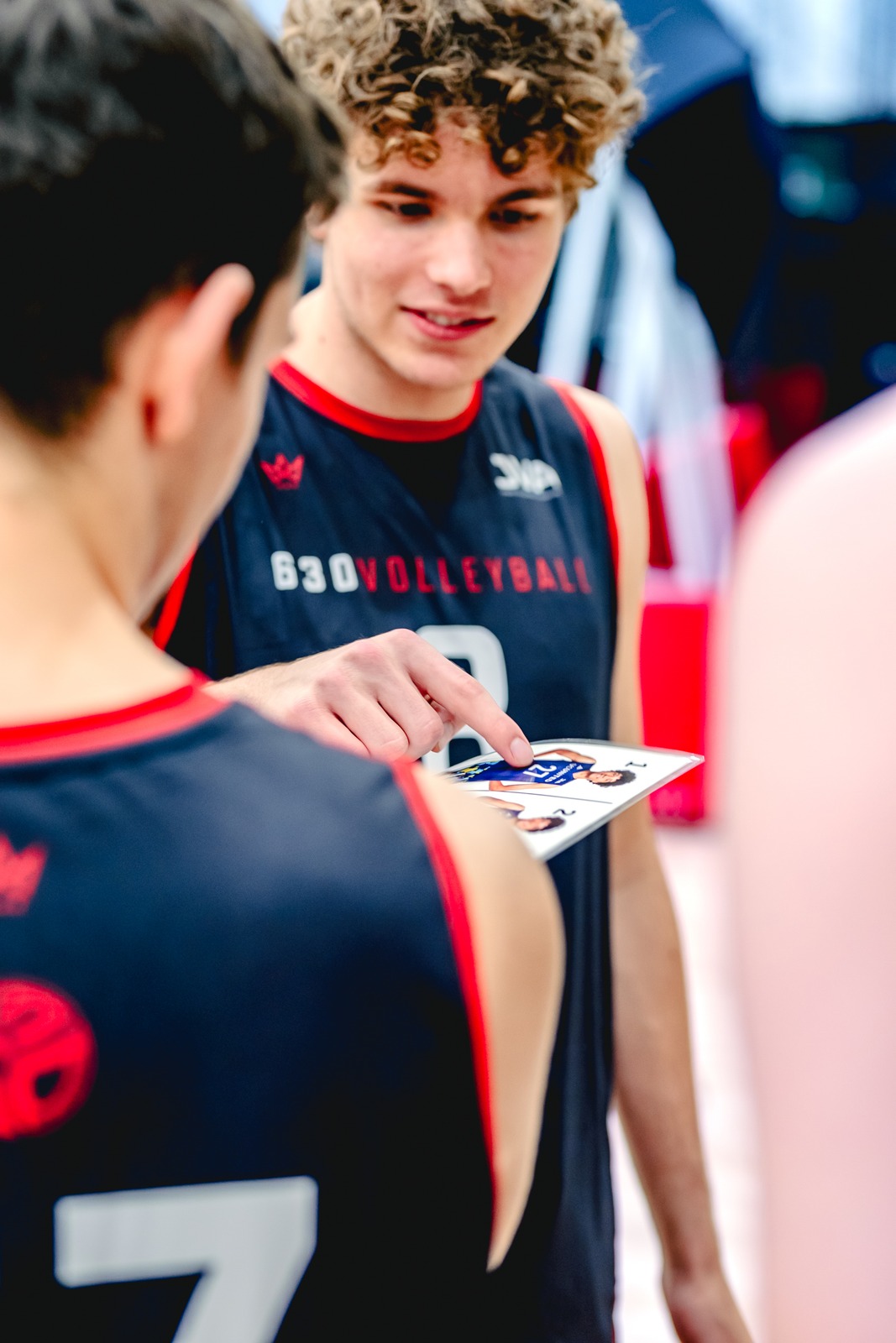 A player in a dark jersey points at a photo sheet while another player faces him.