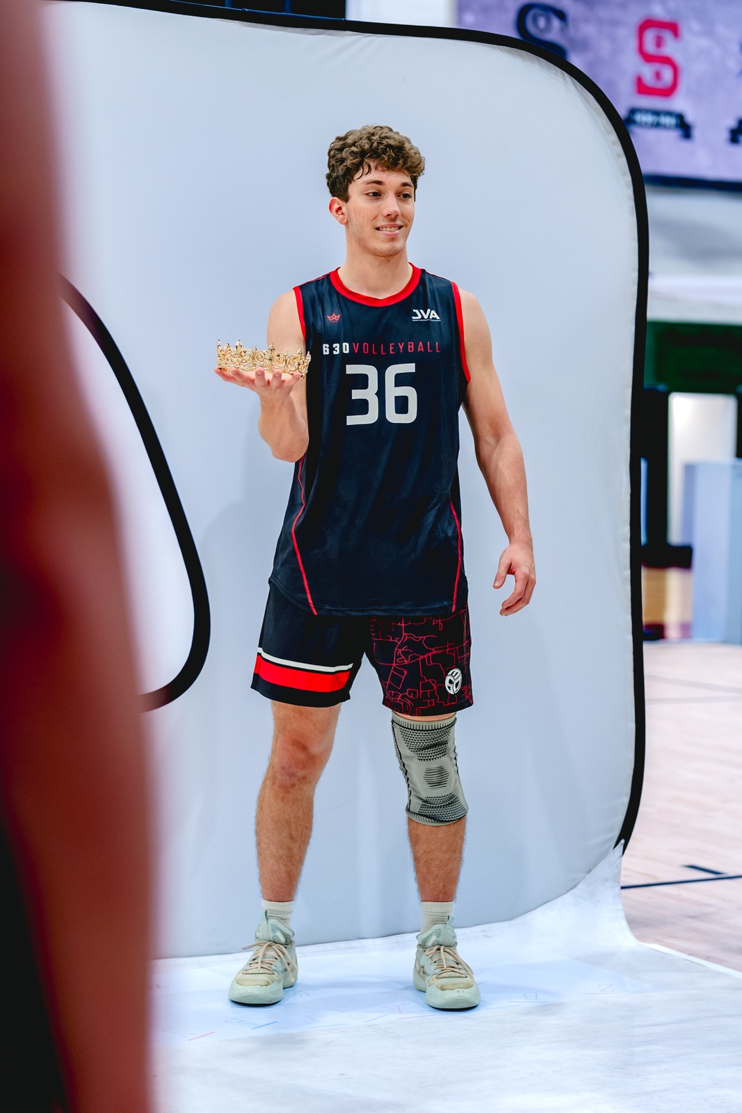 A player in a black jersey and shorts stands holding a crown.
