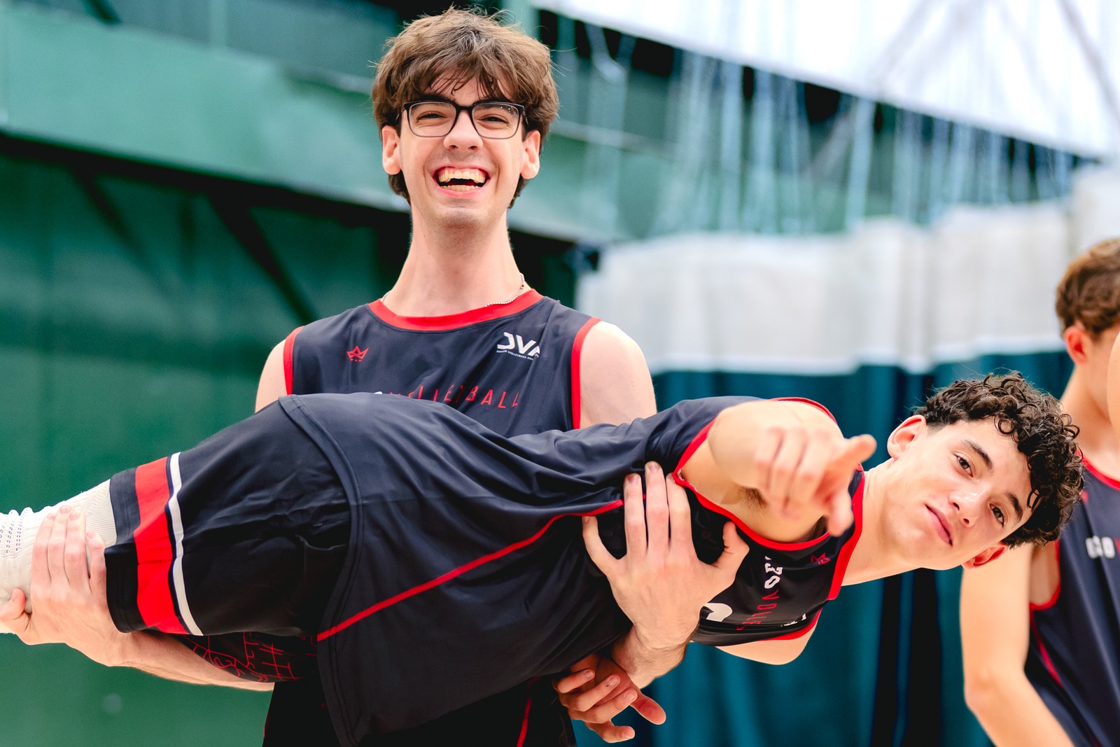 A player in a black top with red trim holds another player in a black top with red trim.