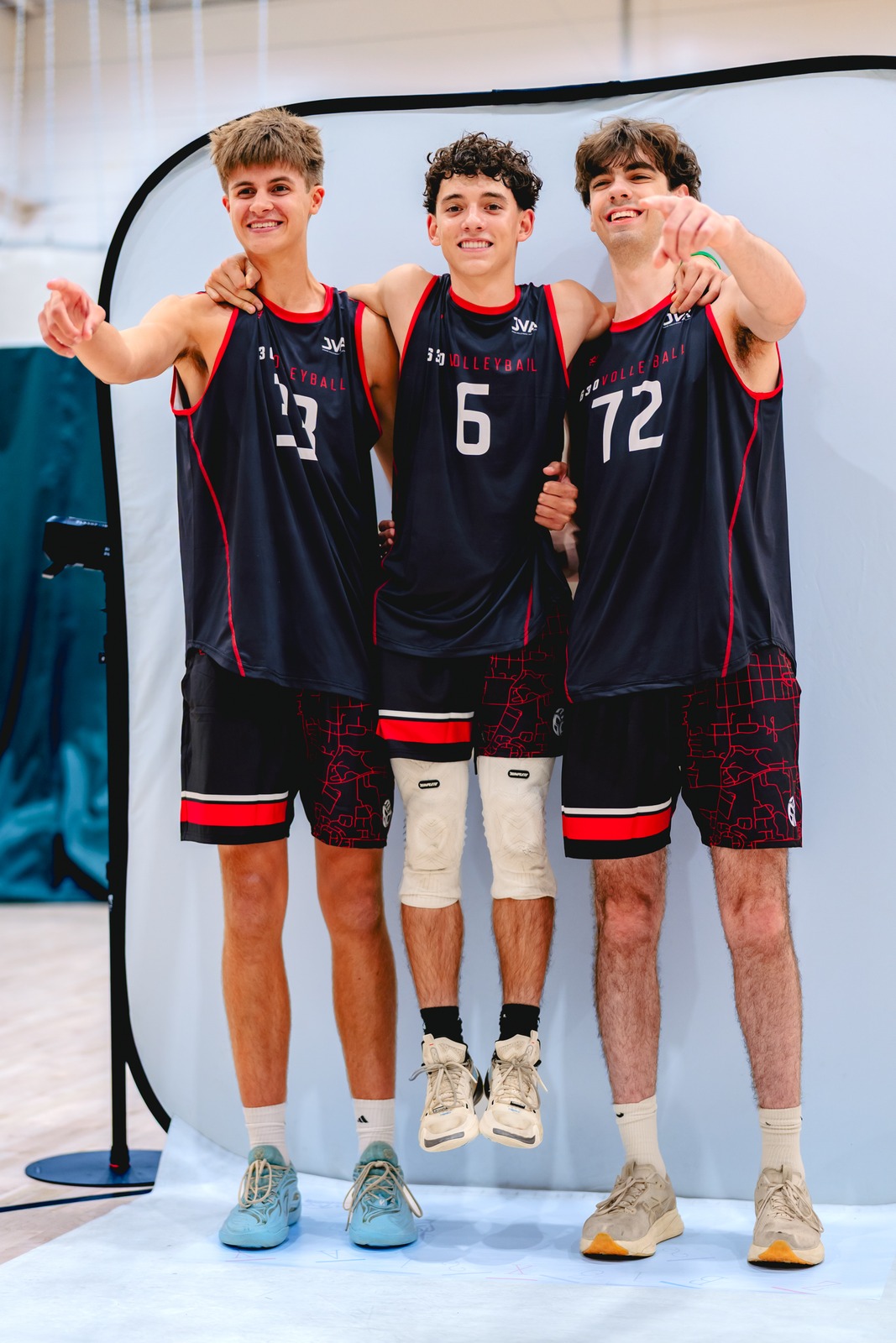 Three players in black jerseys stand together and point forward.