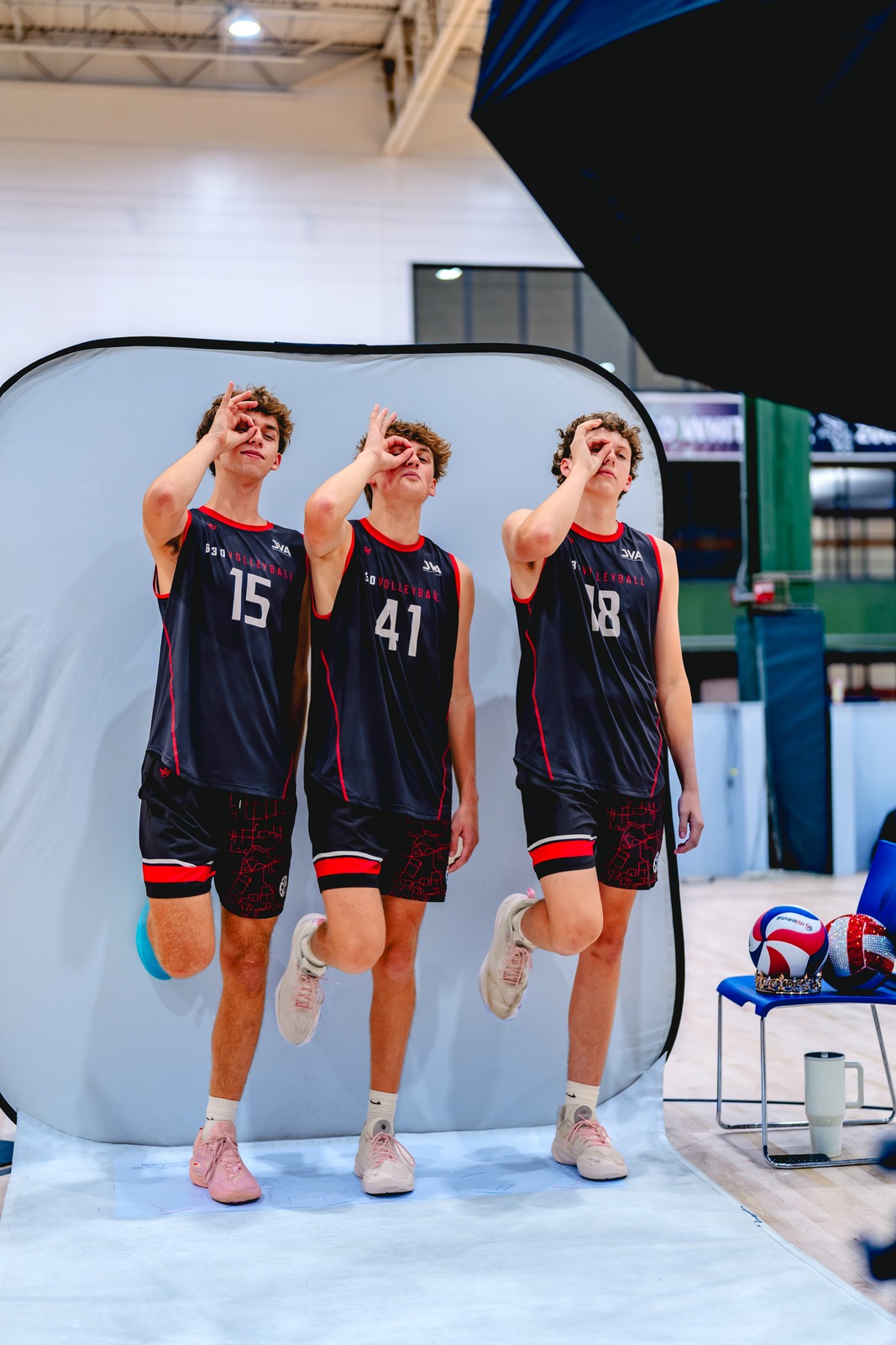 Three players in black and red pose with hand gestures over their eyes.