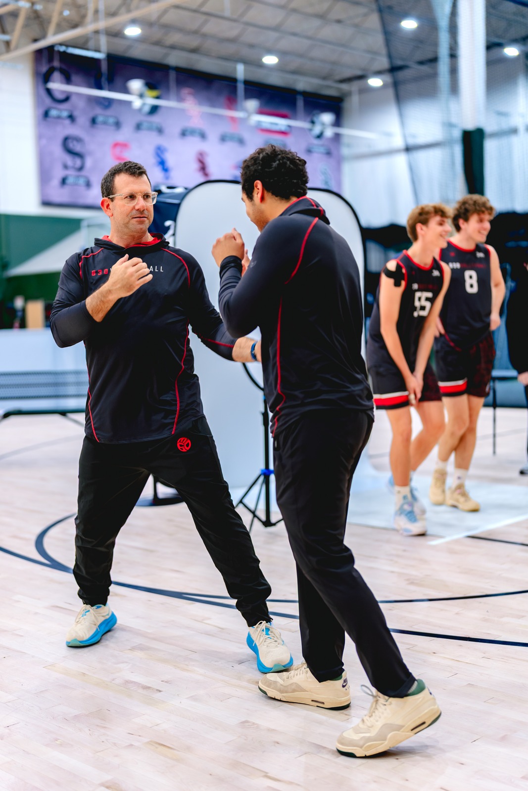A person in a black top with red trim gestures towards another person in a black top.