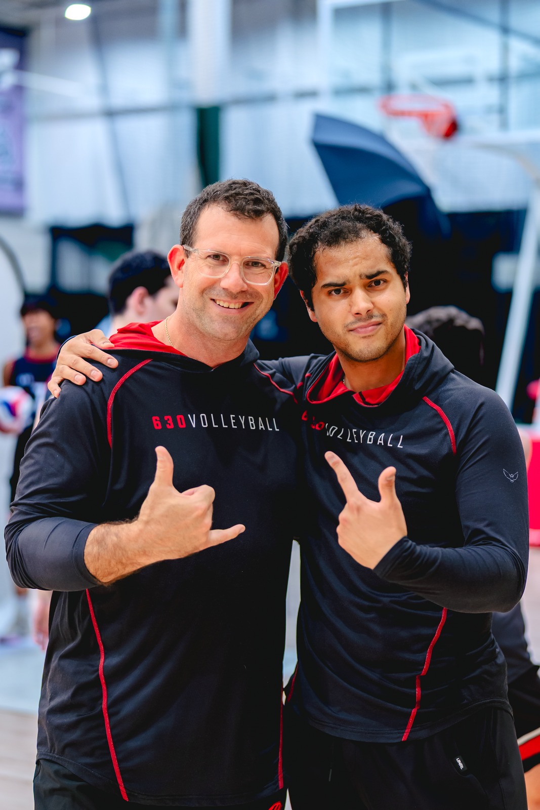 Two people in black tops with red trim pose with arms around each other.