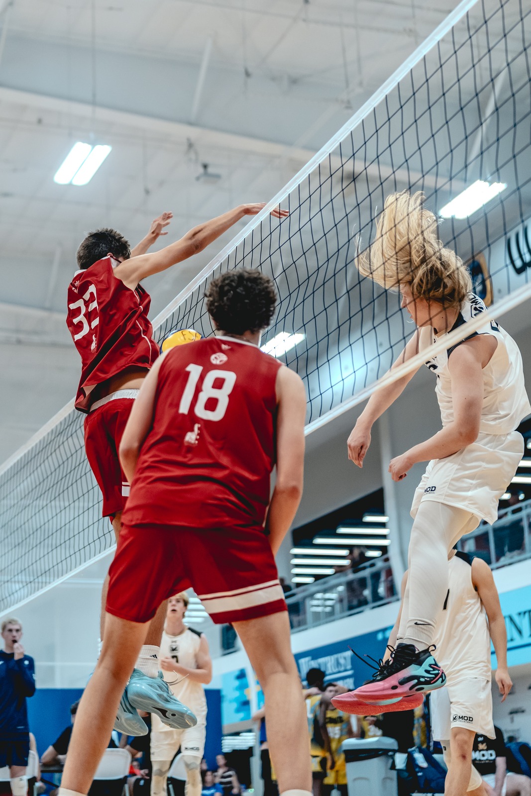 A player in red reaches over the net as a player in white jumps.