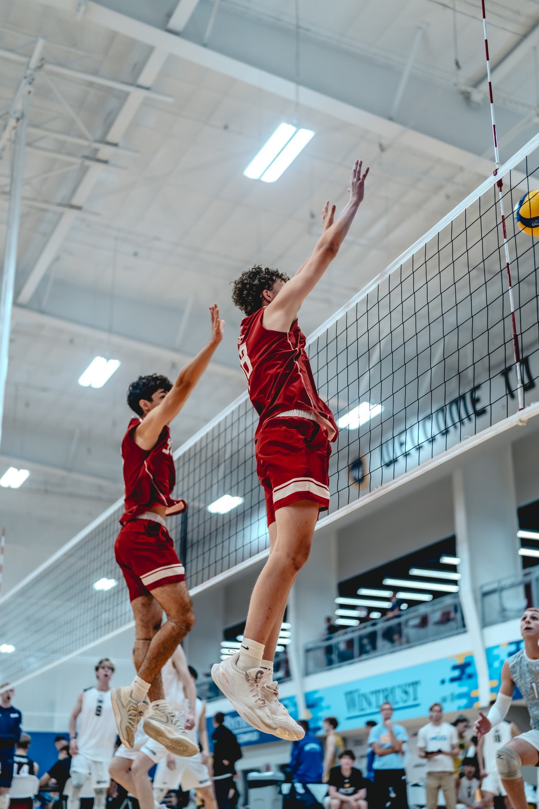A player in red jumps with arms extended, reaching towards the net.