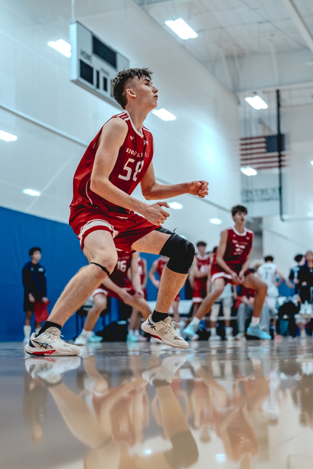 A player in a red uniform crouches low on a court.