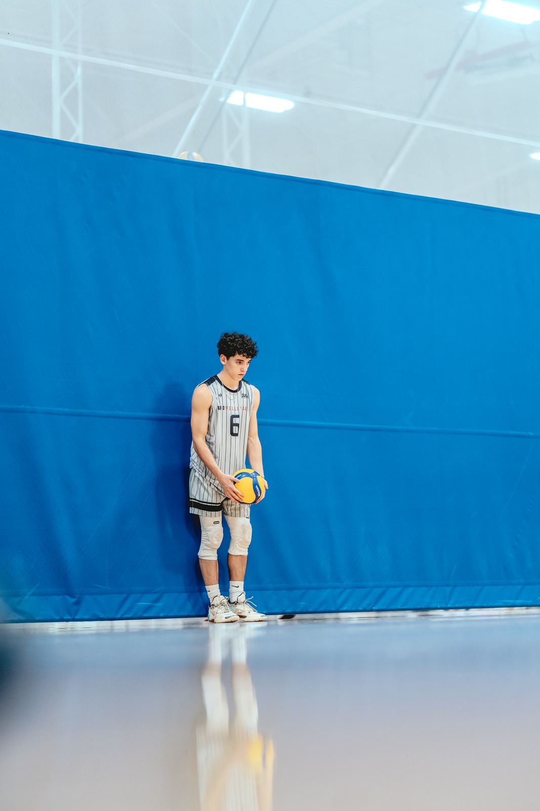 A player in a gray and white uniform holds a volleyball.