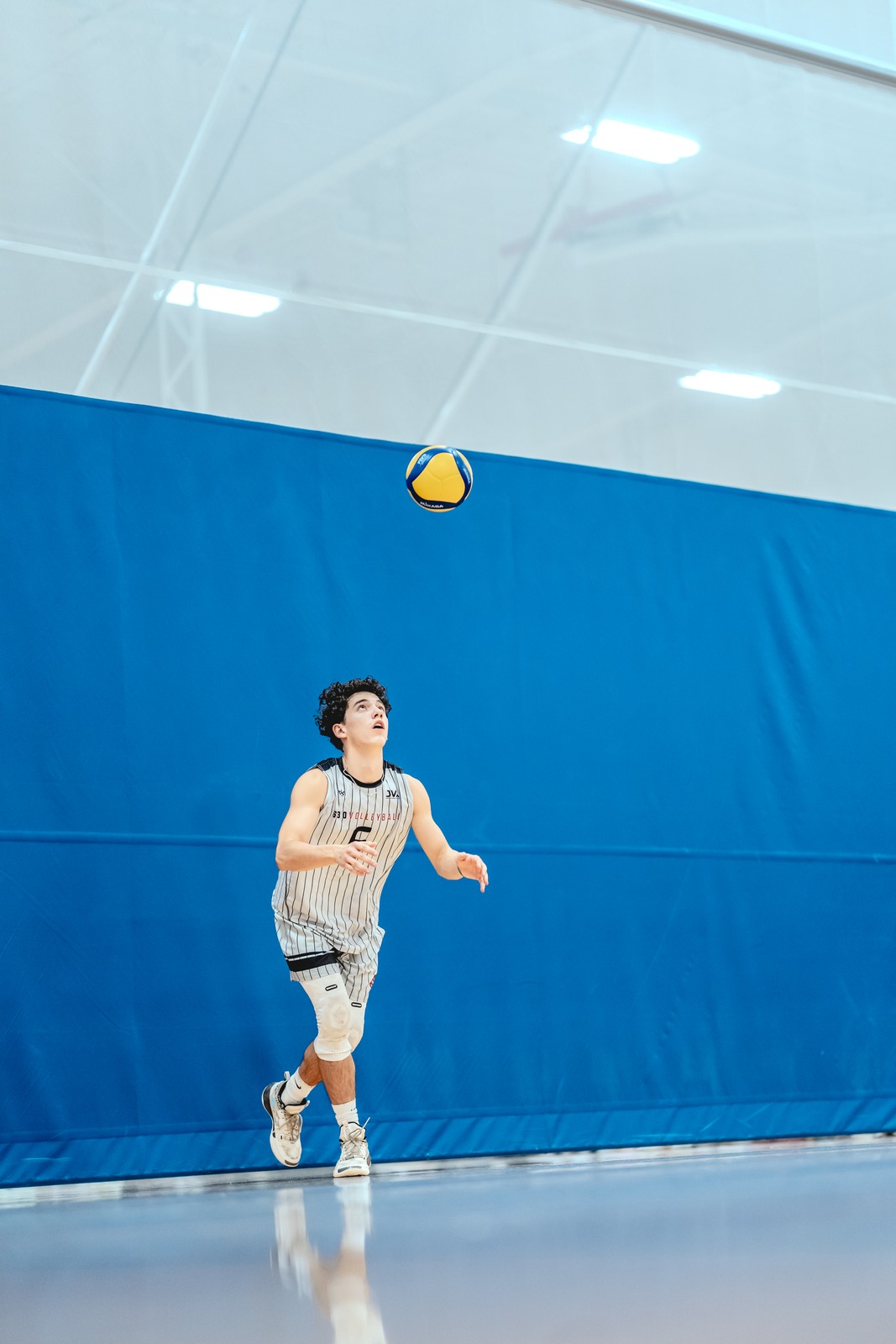 A player in a gray and white striped jersey looks up at the ball.