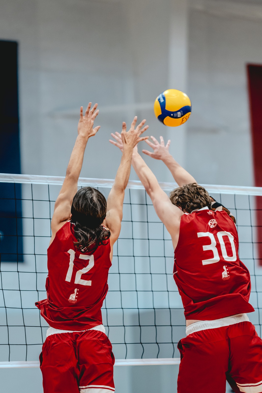Two players in red uniforms reach upwards near a net.