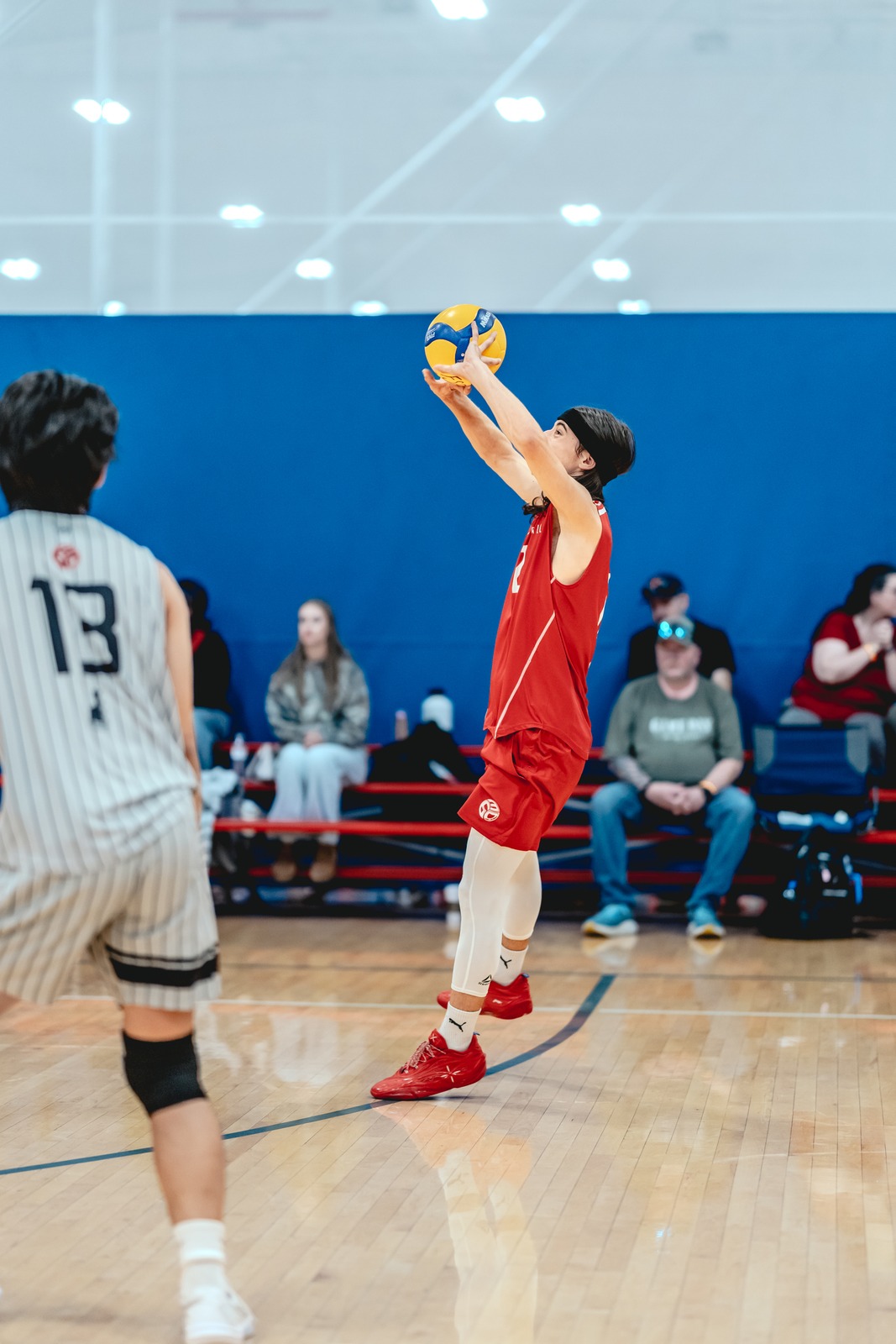 A player in a red top and shorts reaches overhead for the ball.