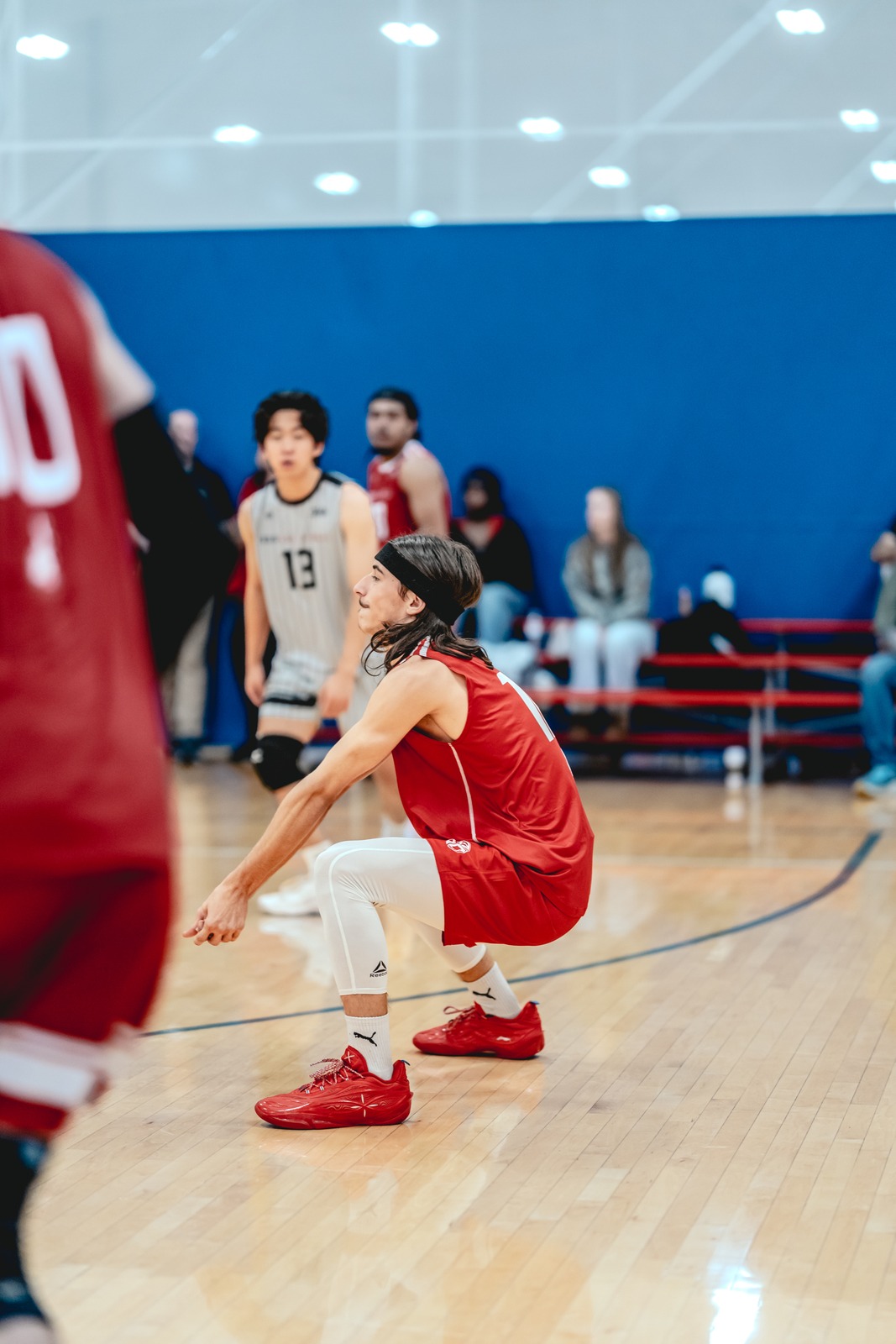 A player in red crouches low on a wooden court.